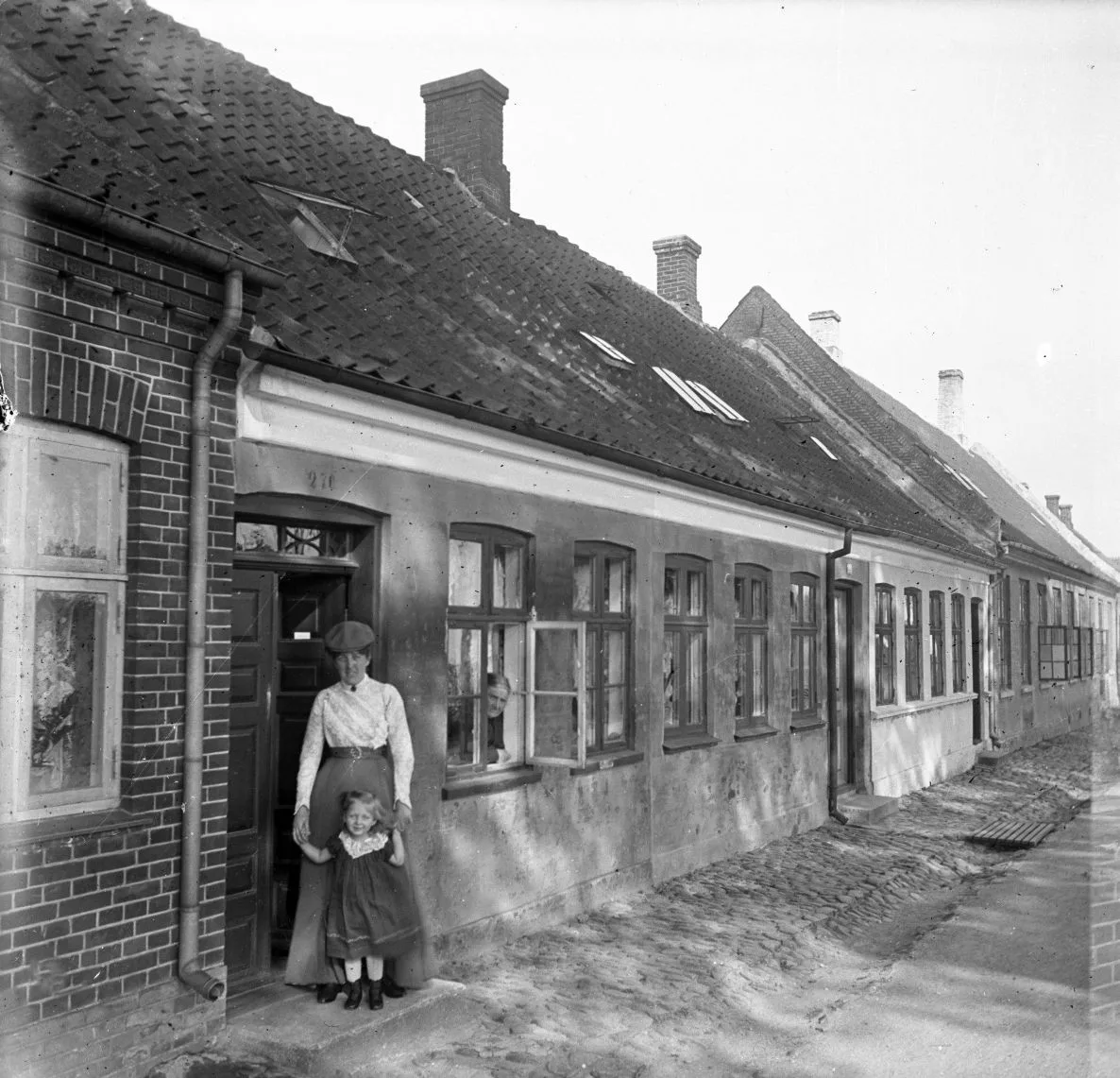 90.33 90.33 Alstrups hustru og datter cirka 1905-06 ved Kongebrovej 18, matr.nr. 270. Der var friskole på det tidspunkt, så Alstrups har sikkert besøgt bekendte. Både Alstrup og hustru var lærere.